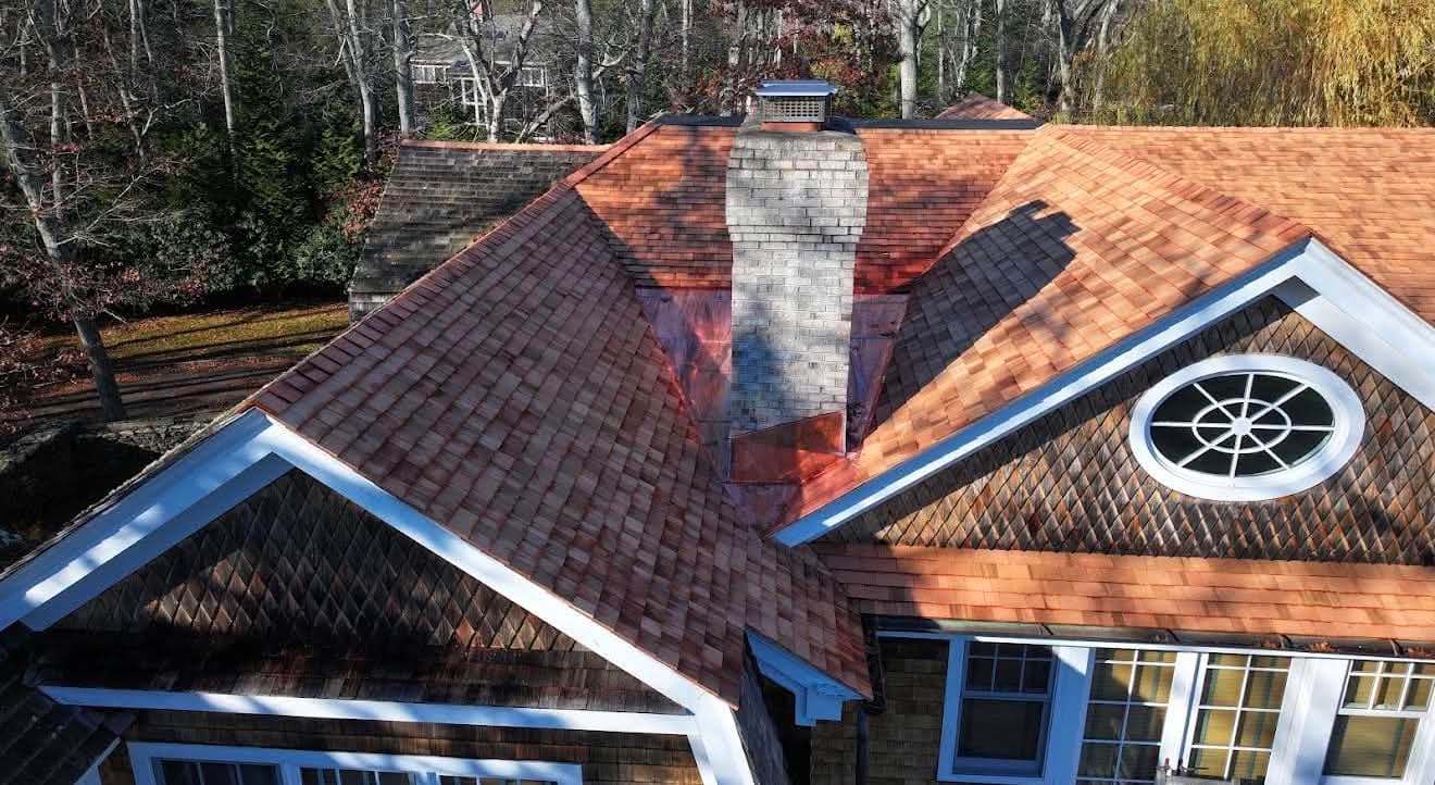 Aerial view of a finished cedar shake roof with new copper flashing wrapped around a brick chimney