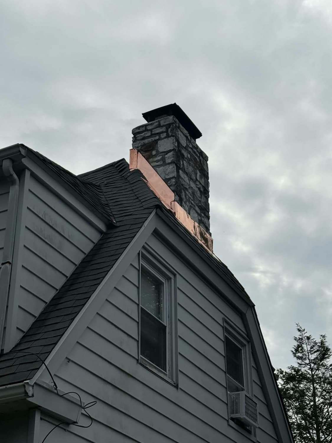 Chimney with new copper flashing at the roofline of a Bryn Mawr, PA home with grey siding