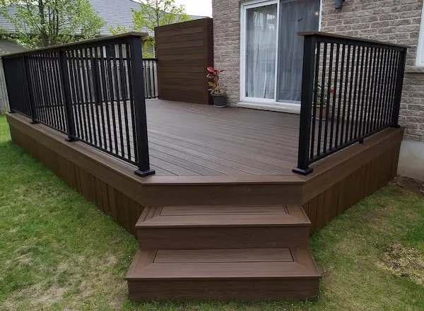 Brown composite deck with black metal railings and wide steps down to the lawn