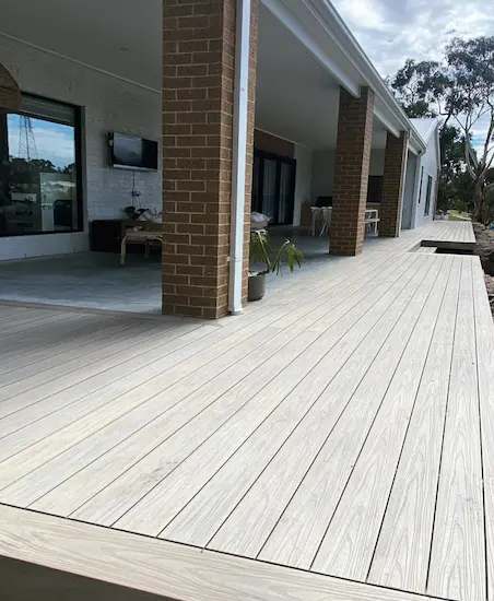Light grey composite deck boards running under a covered porch roof beside a brick column