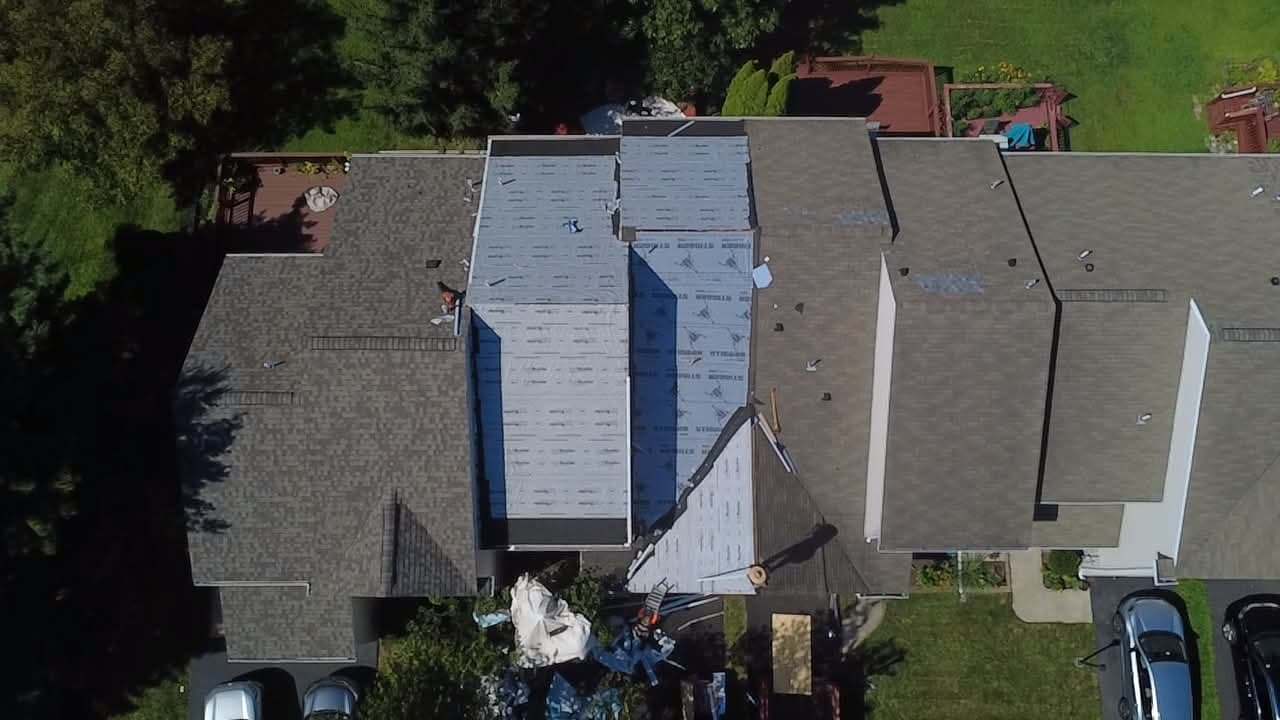 Overhead drone view of a roof mid-replacement, with new synthetic underlayment down across one section and old shingles still on the rest