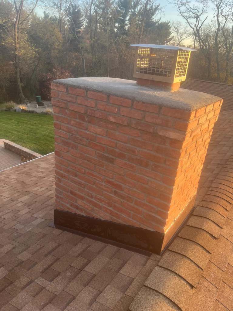 Rebuilt brick chimney with a fresh crown and a stainless steel cap, seen from the roof