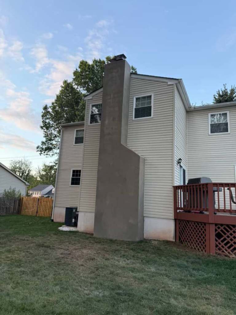 Stucco-covered chimney chase running up the back of a two-story house, with a red deck beside it