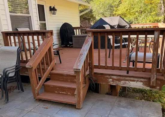 Weathered wood deck and stairs with peeling red stain and worn railings, patio furniture behind