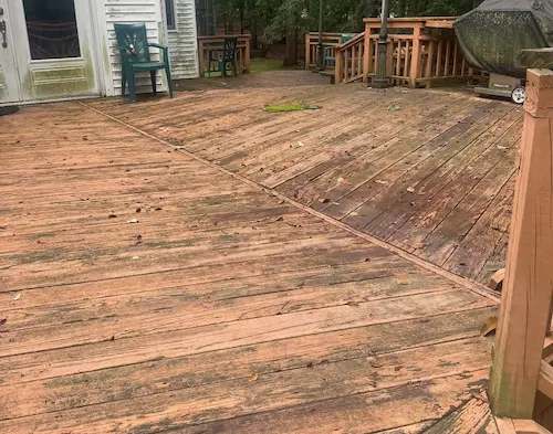 Weathered wood deck boards with moss and worn stain beside the back of a house